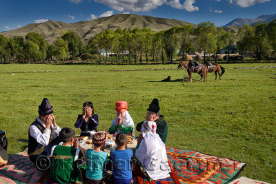 Kazakh family in traditional clothes ending a prayer before a picnic meal in pastureland at Saty Kazakhstan