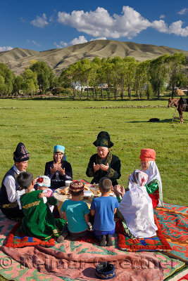 Kazakh family in traditional clothes praying before a picnic meal in pastureland at Saty Kazakhstan