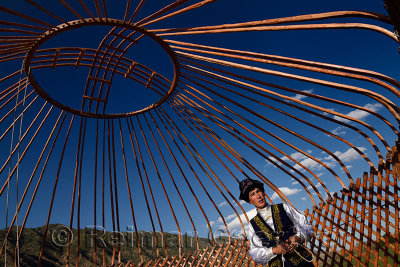 Kazakh man in traditional clothes under the wood frame of a Yurt against a blue sky Saty Kazakhstan
