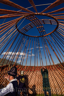 Men in traditional clothes pulling felt rug covers over wood frame of Yurt in Saty Kazakhstan