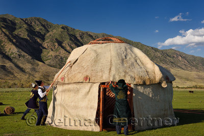 Men in traditional dress fit wool felt covers over Yurt roof frame in Saty Kazakhstan