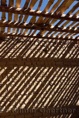 Shadow stripes of timber ceiling beams and slats on mud brick wall at unfinished house near Shymkent Kazakhstan