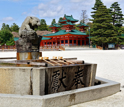 Statue of a lion sits over dippers and a water basin, at Heian Shrine