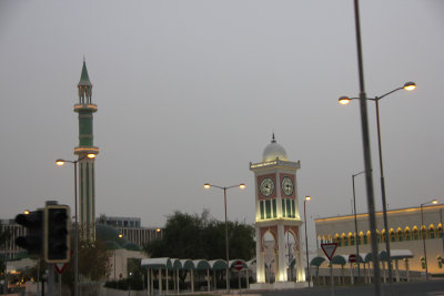 Green minaret of the Grand Mosque and the Clock Tower illuminated at dusk.