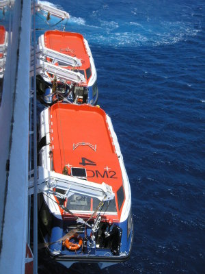 Tenders are going over the side of the ship, which is anchored, to take passengers on shore