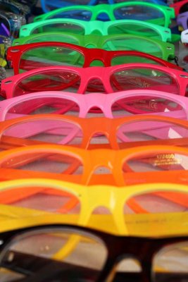 Neon-colored unglasses for sale at a sidewalk display.
