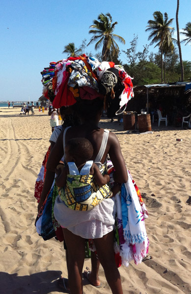 Beach vendor with a kid strapped to her back