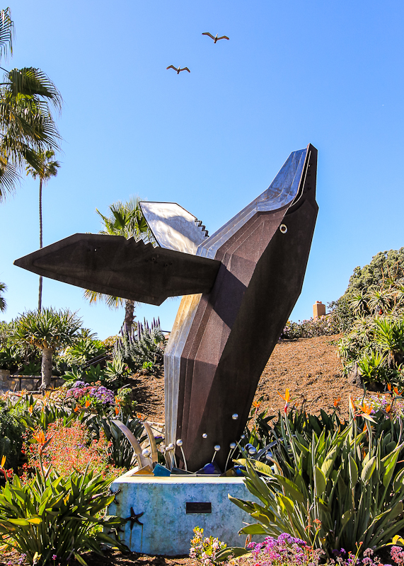 Birds flying over the breaching whale statue in Laguna Beach