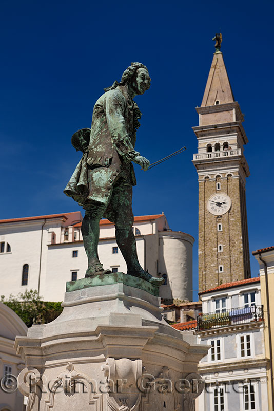 Close up of violinist Giuseppe Tartini statue in Tartini Square Piran Slovenia with St Georges Parish church and bell clock tow