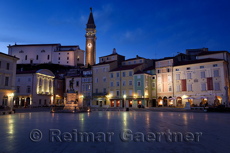 Lights reflected on Tartini Square Plaza in Piran Slovenia with Tartini statue monument, St. Georges Parish Church with belfry 