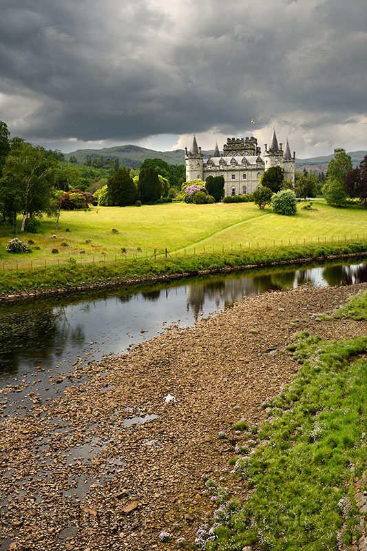 Inveraray Castle in sun reflected in the River Aray at Loch Fyne with dark clouds and sunshine in the Scottish Highlands Scotlan