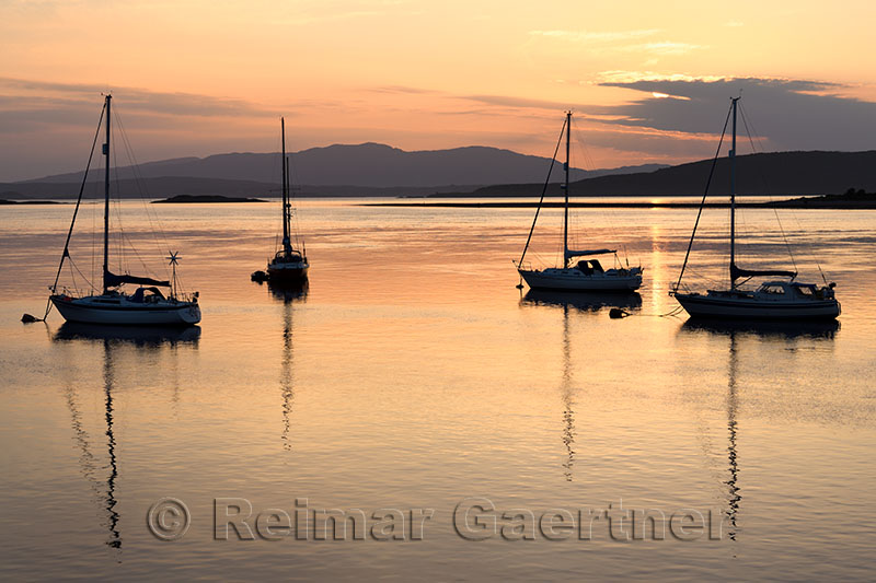 Red sky at sunset over Ardmucknish Bay at North Connel and Oban Airport with sailboats in silhouette