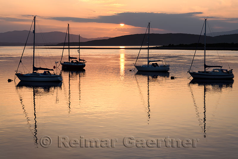 Red sky at sunset reflecting on the water of Ardmucknish Bay at North Connel and Oban Airport with sailboats in silhouette