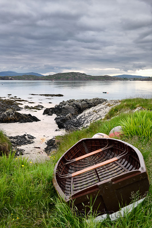 Sand beach and rocky shore of Isle of Iona with beached boat and view of Fionnphort Isle of Mull Sound of Iona Inner Hebrides Sc