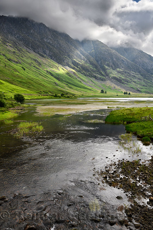 Loch Achtriochtan on the River Coe with dappled sun on the steep Aonach Eagach Ridge mountains in clouds Glen Coe Valley Scotlan