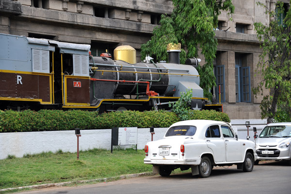 Steam locomotive in front of the Railway Planning Division together with an old white Ambassador