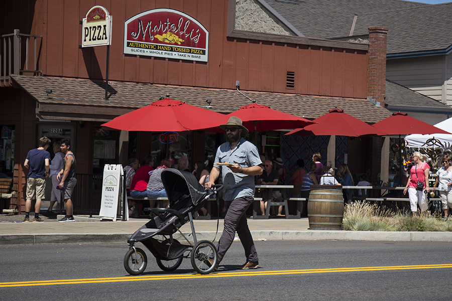 Pushing a baby stroller and carrying a slice of pizza.