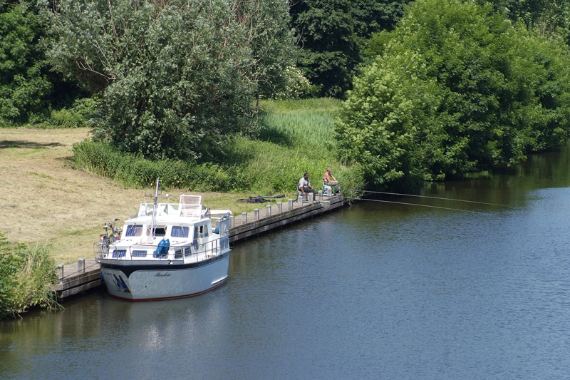 two men with long poles and one boat beside the canal
