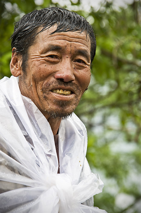 A farmer uses a plastic sheet to keep dry in the drizzly weather