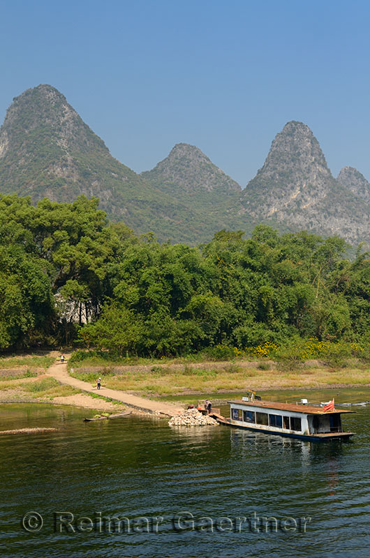 Farmers carrying goods to a bamboo raft with rusted barge and karst peaks on Li river China