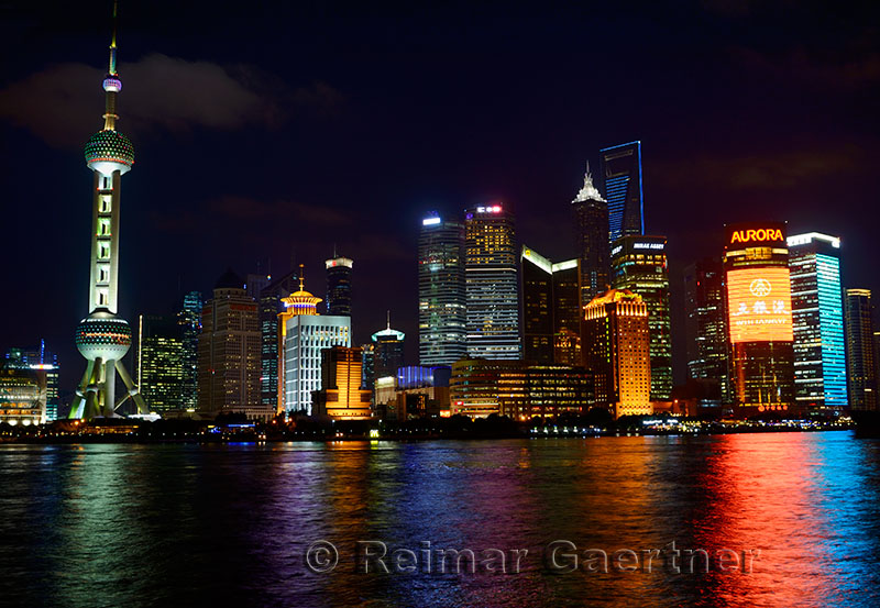 Bright lights of Pudong high rise towers at night reflected in the Huangpu river Shanghai China