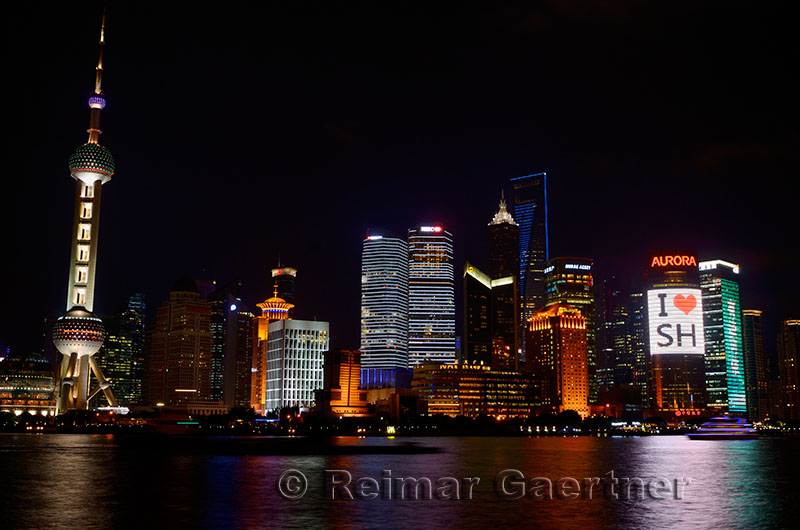 I love Shanghai lights of Pudong high rise towers at night with boats on the Huangpu river China