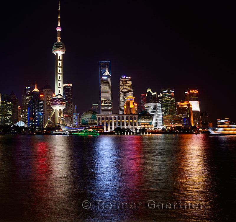 Bright night lights of Pudong high rise towers reflected in the Huangpu river with boats Shanghai China