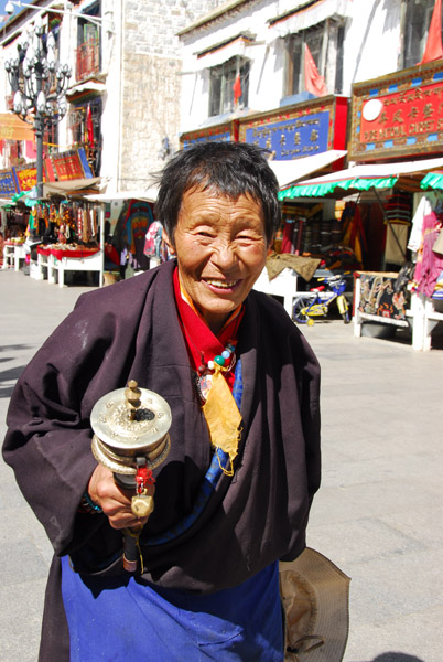 Smiling Tibetan pilgrim on the Barkhor Circuit spinning a prayer wheel