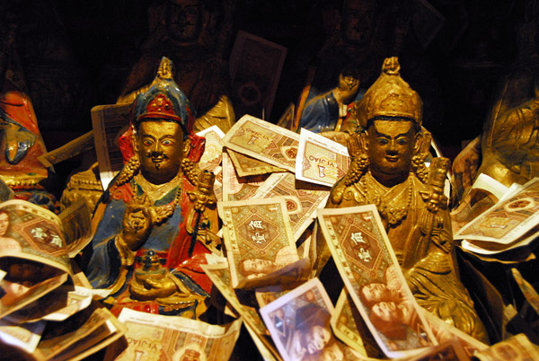 Small statues covered with offerings of small Chinese banknotes