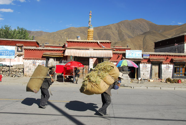 Tibetans carrying large burdens past Trandruk (Chang Zhu) Monastery