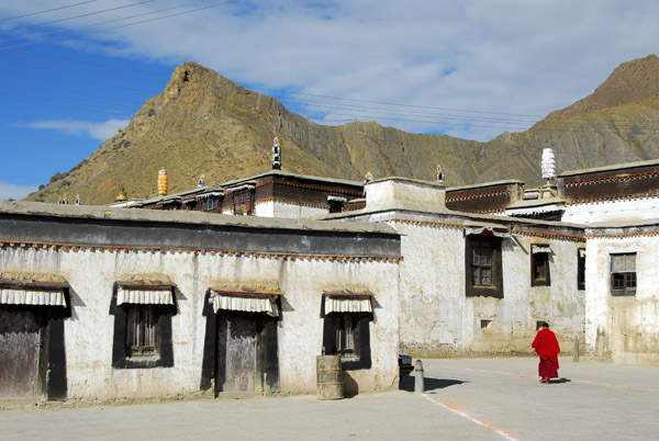 Tibetan monk in red stands out against the white wash of Tashilhunpo Monastery