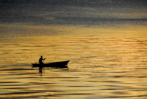 Boy paddling a small boat at sunset, Lake Taal