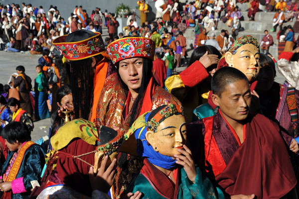Masked characters and men with hats of long hair, Tsechu Festival