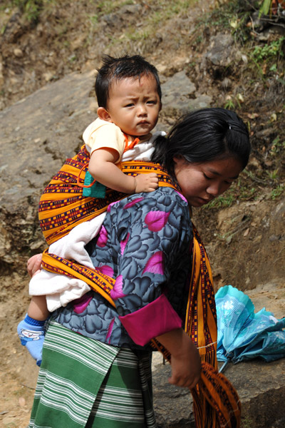 A young woman climbs with a baby strapped to her back