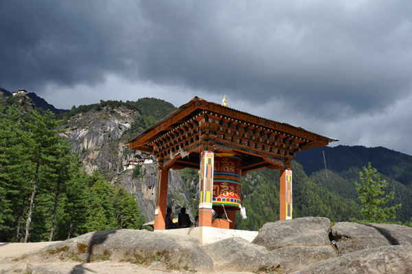Dark clouds above as the sun still shines on the large prayer wheel pavilion