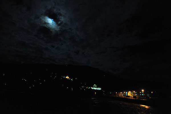 The moon tries to break through the clouds above the lights of Paro