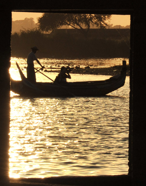 Boat on the lake through pillars of the Teak Bridge at sunset