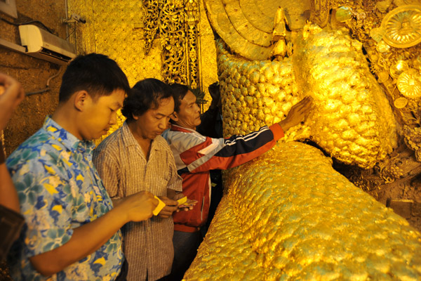 Devote Burmese Buddhist applying additional gold leaf to the Mahamuni Buddha image