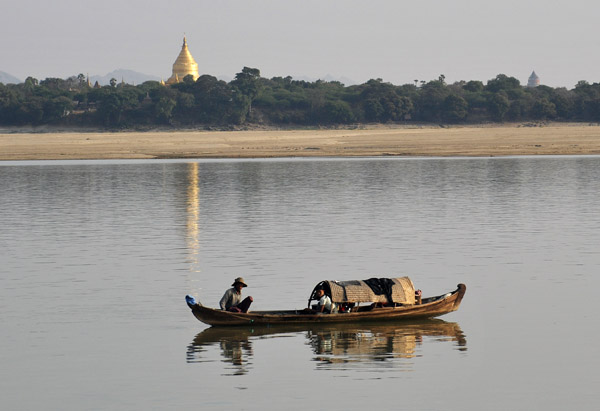 Small boat on the Irrawaddy River with the gold-covered stupa of Shwezigon Paya