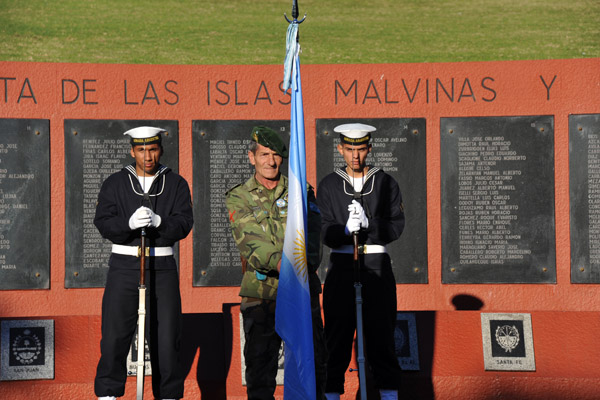 Two sailors stand with a veteran holding the Argentine flag at the Malvinas Memorial