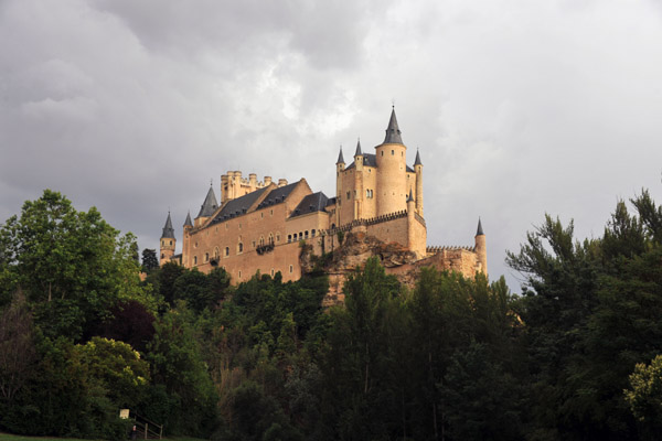 Alcazar of Segovia rising above the trees with a stormy sky