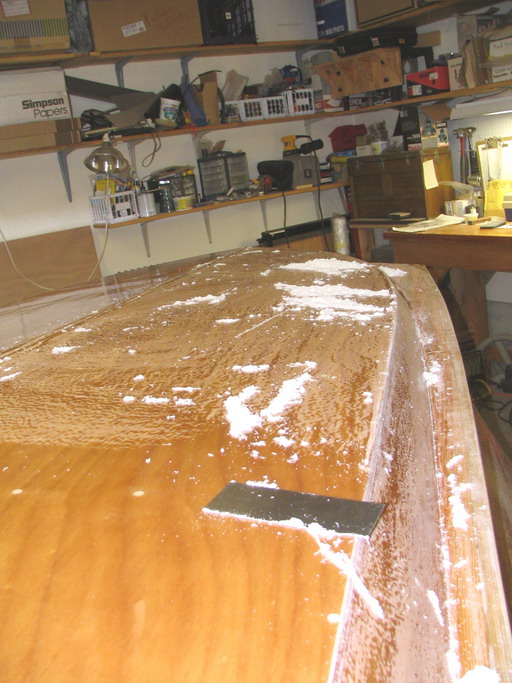 Scraping excess resin after two fill coats; saves sanding; best done before full cure.