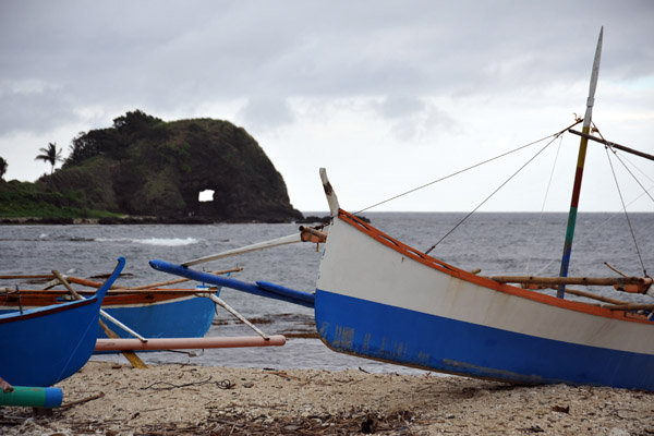 Outrigger fishing boat pulled up on the beach with Bantay Abot Cave in the background