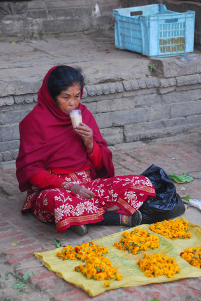 Woman with a glass of hot tea selling flowers, Taumadhi Tole