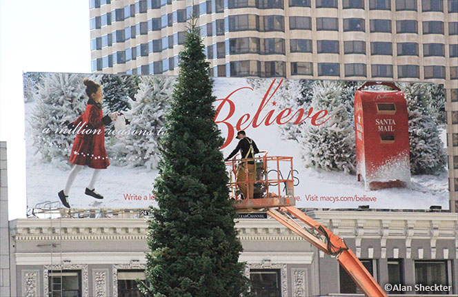 Worker preps Christmas tree with seasonal Macys billboard as a backdrop