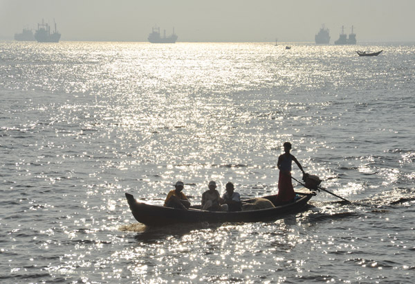 Morning sun reflections silhouetting a Burmese long-tail boat, Yangon River estuary