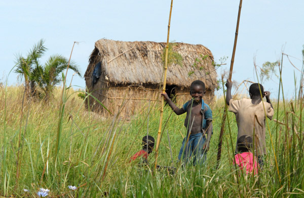 Boys with bamboo poles in front of their grass hut, Bangweulu Swamps