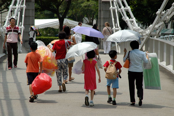 Pedestrians crossing the Cavenagh Bridge with umbrellas for protection from the hot sun