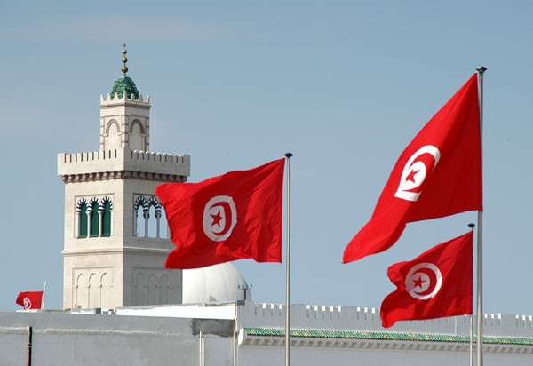 Tunisian flags flying over Place de la Kasbah with the minaret of the Kasbah Mosque
