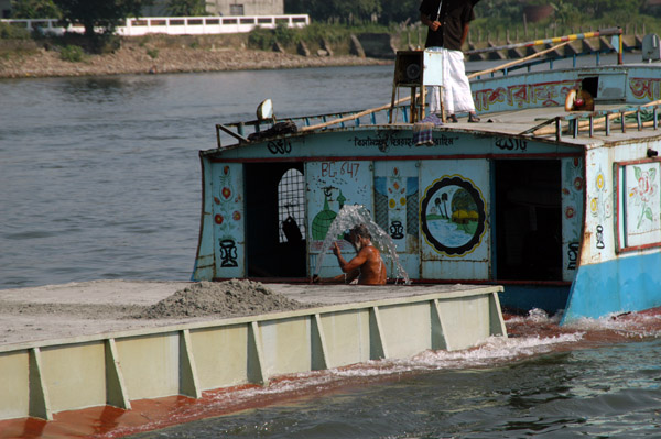 Sailor manning the pumps of an overloaded sand freighter on the Buriganga River, Bangladesh